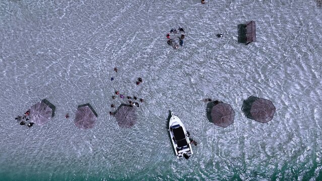 Aerial view of Banco de arenas Grand Grossier with people under thatched umbrellas in shallow turquoise water and a motorboat moored nearby in Monte Cristi, Monte Cristi, Dominican Republic.