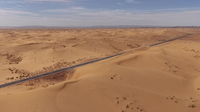 Aerial Top View of a Car Driving Along a Desert Road Surrounded by Golden Sand Dunes
