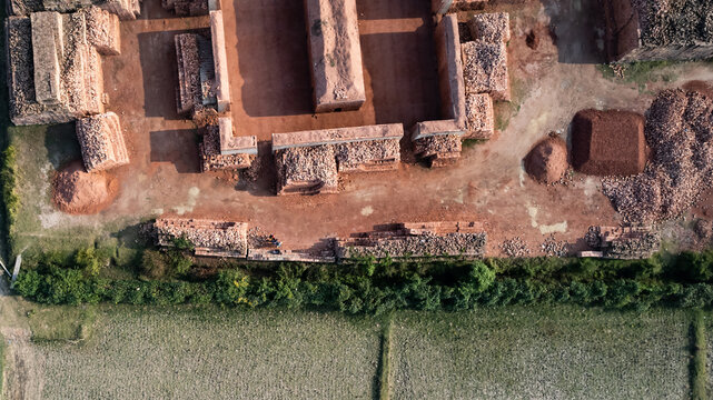 Aerial view of a brick kiln with organized stacks of red clay bricks, piles of raw materials, and surrounding green agricultural fields in Chittagong, Chattogram, Bangladesh.