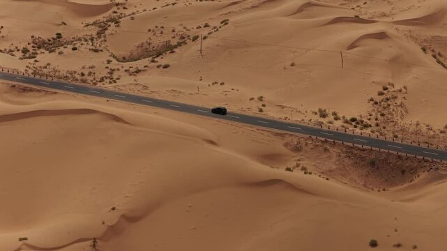 Aerial Top View of a Car Driving Along a Desert Road Surrounded by Golden Sand Dunes
