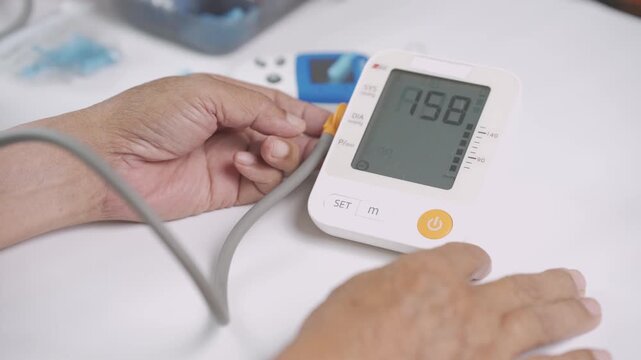 Close-up of a senior adult using a digital blood pressure monitor at home to check blood pressure and heart health. Healthcare monitoring, hypertension prevention, home care.