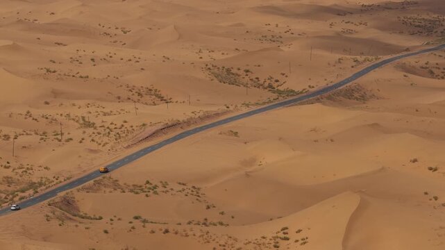 Aerial Top View of a Car Driving Along a Desert Road Surrounded by Golden Sand Dunes