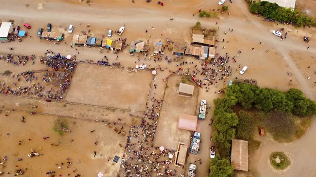 Top-down drone footage of the bustling Maasai livestock market in Kimana, Kenya, showing traders loading goats onto trucks and the adjacent highway to Nairobi.
