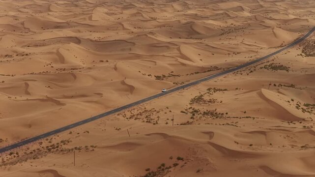 Aerial Top View of a Car Driving Along a Desert Road Surrounded by Golden Sand Dunes