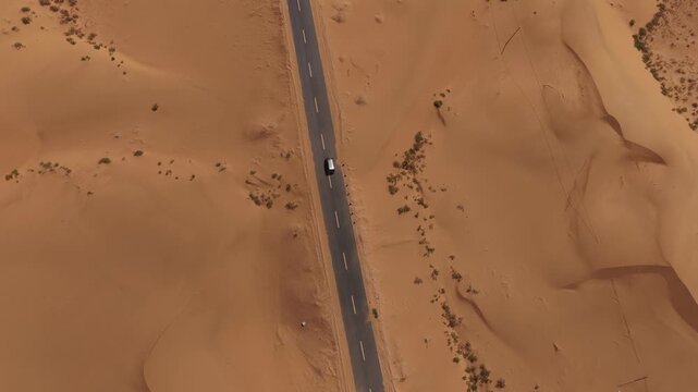 Aerial Top View of a Car Driving Along a Desert Road Surrounded by Golden Sand Dunes