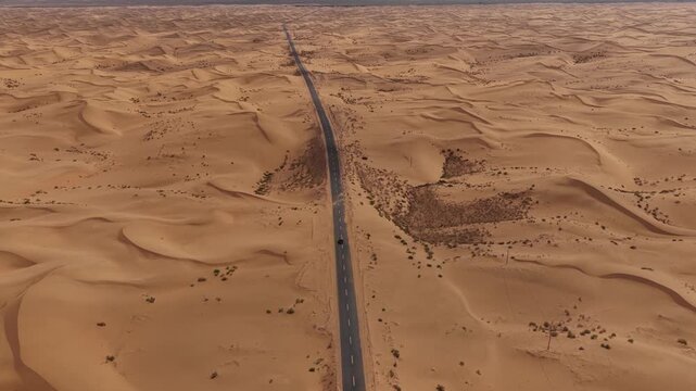 Aerial Top View of a Car Driving Along a Desert Road Surrounded by Golden Sand Dunes