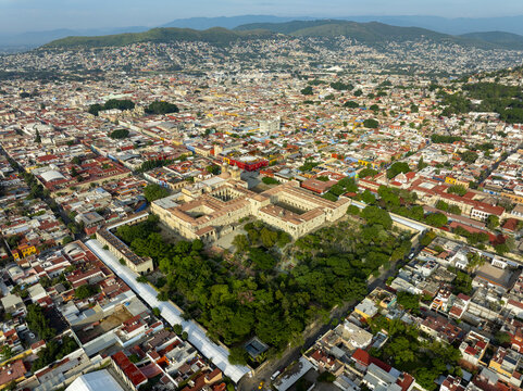 Aerial view of the historic Templo de Santo Domingo de Guzman surrounded by colonial rooftops, lush gardens, and the urban landscape of Oaxaca de Juarez, Oaxaca, Mexico.