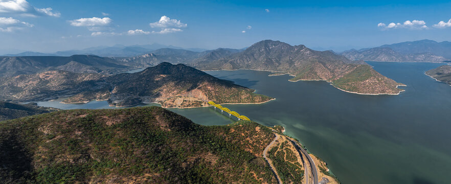 Aerial view of the yellow bridge crossing the Rio Balsas reservoir surrounded by rugged mountains and lush vegetation in Infiernillo, Michoacan, Mexico.