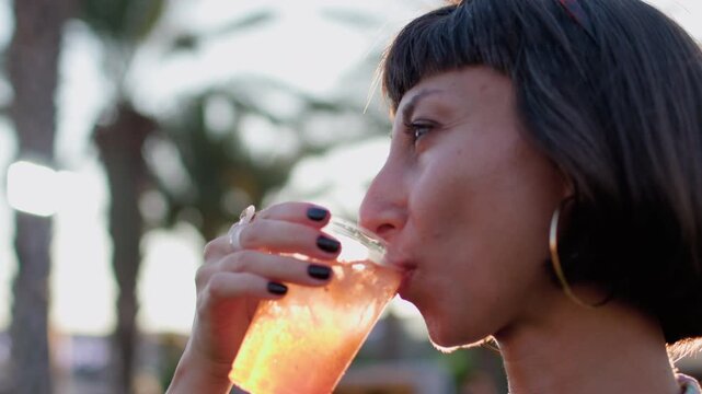 The joyful young woman laughs outdoors with a cocktail in her hands. party at sunset. summer celebration. summer festival. girl with a cocktail outside