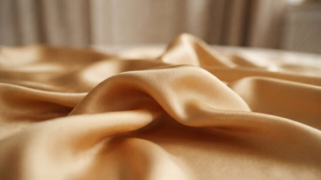 Soft light gold silk satin fabric folds, luxurious smooth textile texture background