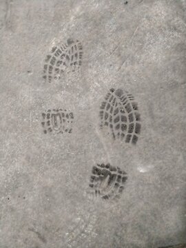 Wet shoe boot sole footprints stamped on a concrete floor surface