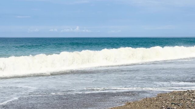 Blue sea and large waves and foam. Wave splashing over pebbles at sea. Rolling ocean waves. Summer beach background. Powerful sea waves	