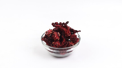 A small glass bowl filled with dried dark red roselle hibiscus flowers, isolated on a clean white background. © VH_World