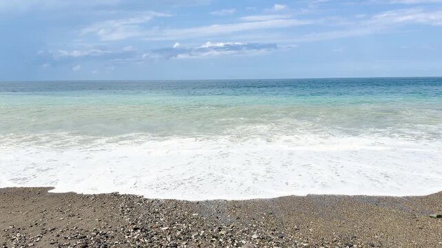 Blue sea and large waves and foam. Wave splashing over pebbles at sea. Rolling ocean waves. Summer beach background. Powerful sea waves	