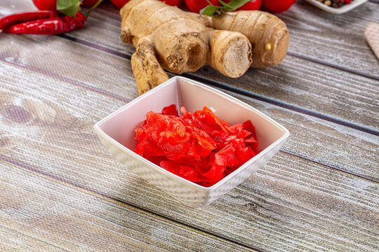 Pickled ginger in white bowl with fresh ginger root and red chili peppers on rustic wood table