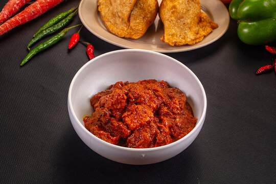Spicy red curry paste in white bowl with fried snacks and fresh chilies on dark surface