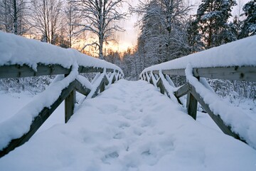 Obraz premium The Snowy Bridge Through A Quiet Winter Forest at Sunset