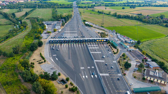 Aerial view of Barriera A7 Milano Ovest toll plaza with multiple lanes and surrounding agricultural fields in Assago, Lombardia, Italy.