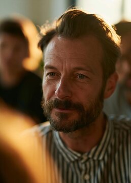 Close-up portrait of a middle-aged man with a beard and mustache. he is looking directly at the camera with a slight smile on his face. he has short, dark hair and is wearing a striped shirt.