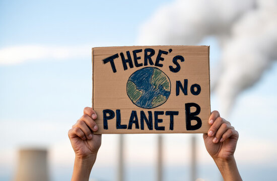 Hands raise a cardboard No Planet B sign against a smoky sky, climate protest, environmental activism, global awareness, public message.