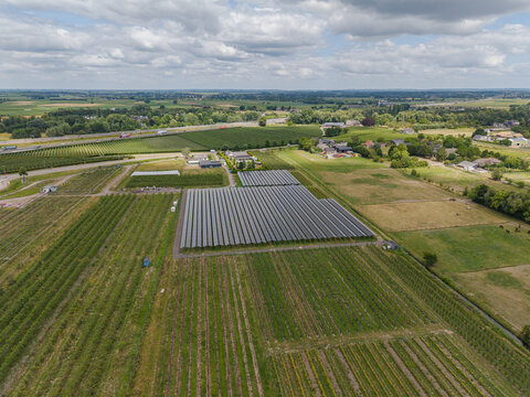 Aerial view of a large solar panel array situated in a rural landscape with surrounding agricultural fields, green meadows, and a distant highway in the Netherlands.