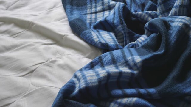 Messy unmade bed with a white quilted protector and blue plaid blanket. Concept of waking up in the morning, unorganized bedroom and daily routine.