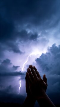Hands clasped in prayer under stormy sky with lightning