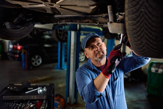 Mature mechanic repairing vehicle suspension system in car service workshop.