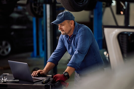 Mature mechanic using computer for car diagnostics in workshop.