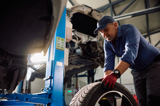Mature technician replacing car tire during vehicle service in garage.