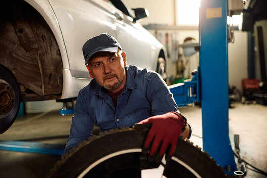 Mature auto mechanic replacing car tire in garage.
