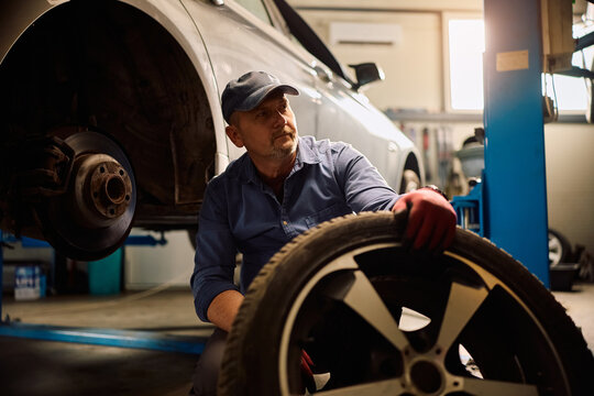 Mature mechanic installing new tire on vehicle at car service.