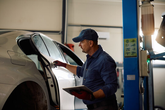 Mature car repair specialist inspecting vehicle in garage.