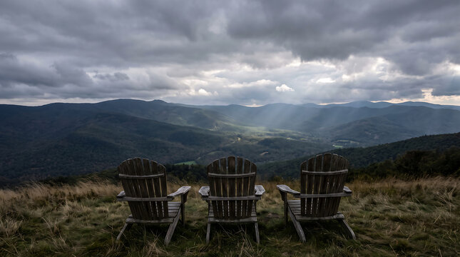 Three wooden chairs on a grassy mountain hill overlooking a scenic valley under cloudy sky