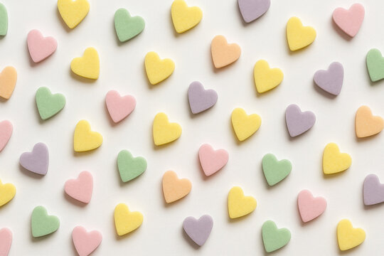 Pastel heart shaped sugar candies scattered on white background create soft and cheerful pattern with yellow, pink, green, purple, and orange colors evoking sweet and playful mood