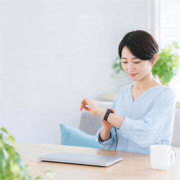 ノートパソコンの前でスマートウォッチを確認する女性