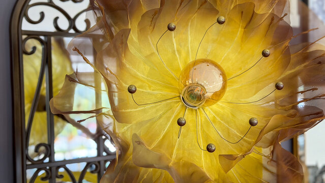 Close-up of decorative flower-shaped lamp with translucent golden fabric petals and glowing light bulb, creative floral lighting design.