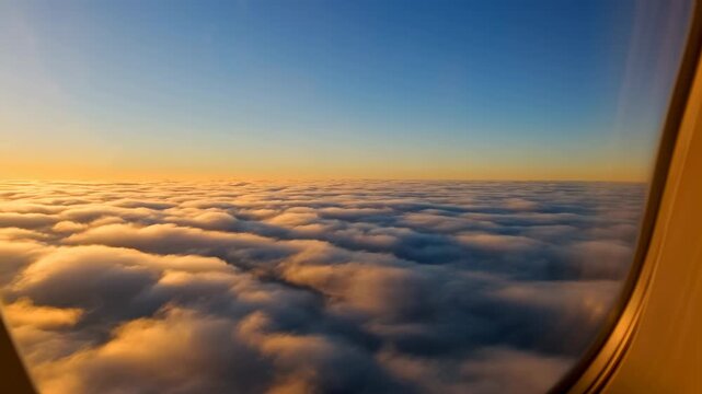 Golden sunrise glow over stratocumulus cloud deck viewed through curved aircraft window from passenger seat above open sky and distant horizon with soft reflections