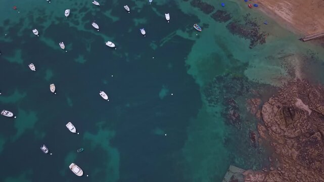 Anchored leisure boats above clear turquoise water and rocky shoreline at Saint-Lunaire beach, Ille-et-Vilaine, Brittany, France, English Channel, Emerald Coast, camera tilted downward, dro
