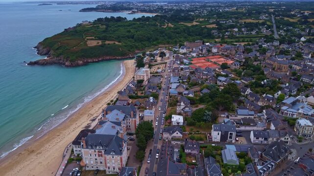 Saint-Lunaire waterfront and Longchamp Beach, Ille-et-Vilaine, Brittany, France, overlooking the English Channel and Emerald Coast with coastal headland, town center and sandy beach, drone pullout.