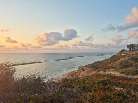 Coastal view at sunset showcasing tranquil ocean waters, rocky shoreline, and vibrant vegetation along the cliffs with a colorful sky and clouds