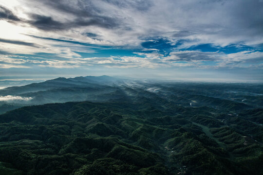 Aerial view of lush green rolling hills and mountains under a dramatic cloudy sky with light rays in Bandarban, Chittagong Division, Bangladesh.