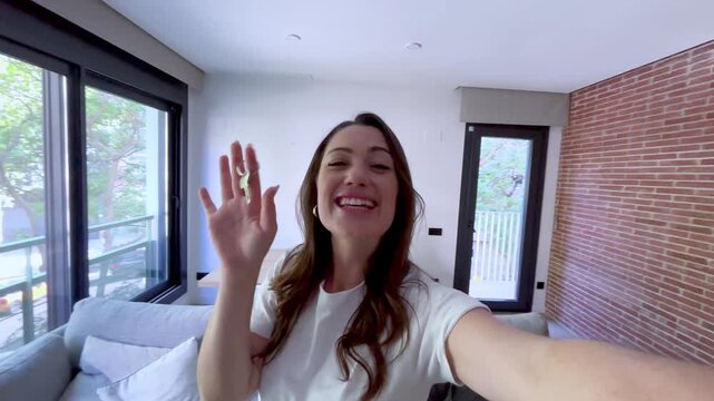 A happy woman joyfully holds up keys in her new, bright apartment, celebrating a significant life milestone like buying a home or moving in. She smiles and gestures, showing her excitement.