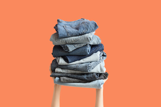 Hands holding a tall stack of folded blue denim jeans in various shades, laundry and clothing organization