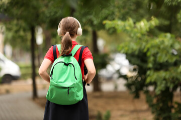 Naklejka premium Young student walking to school with a green backpack and headphones, back to school concept, education and learning