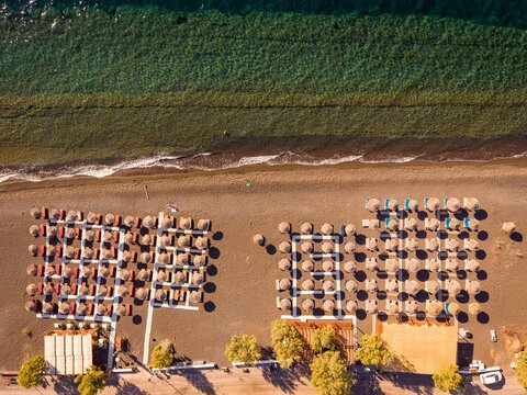 Top down aerial drone view of beach umbrellas and sunbeds on black volcanic sand in Perissa Santorini Greece