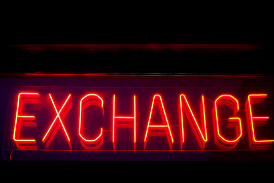 Glowing red neon EXCHANGE sign against a dark background.