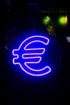 Glowing blue neon Euro symbol sign against a dark background.
