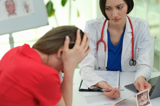 Woman cries as doctor explains ultrasound images bad meaning in clinic. Female physician shows support to despaired patient at appointment in hospital