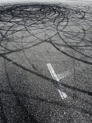 Black tire tracks swirl across asphalt surface. Pattern suggests vehicle maneuvering or drifting. © schankz